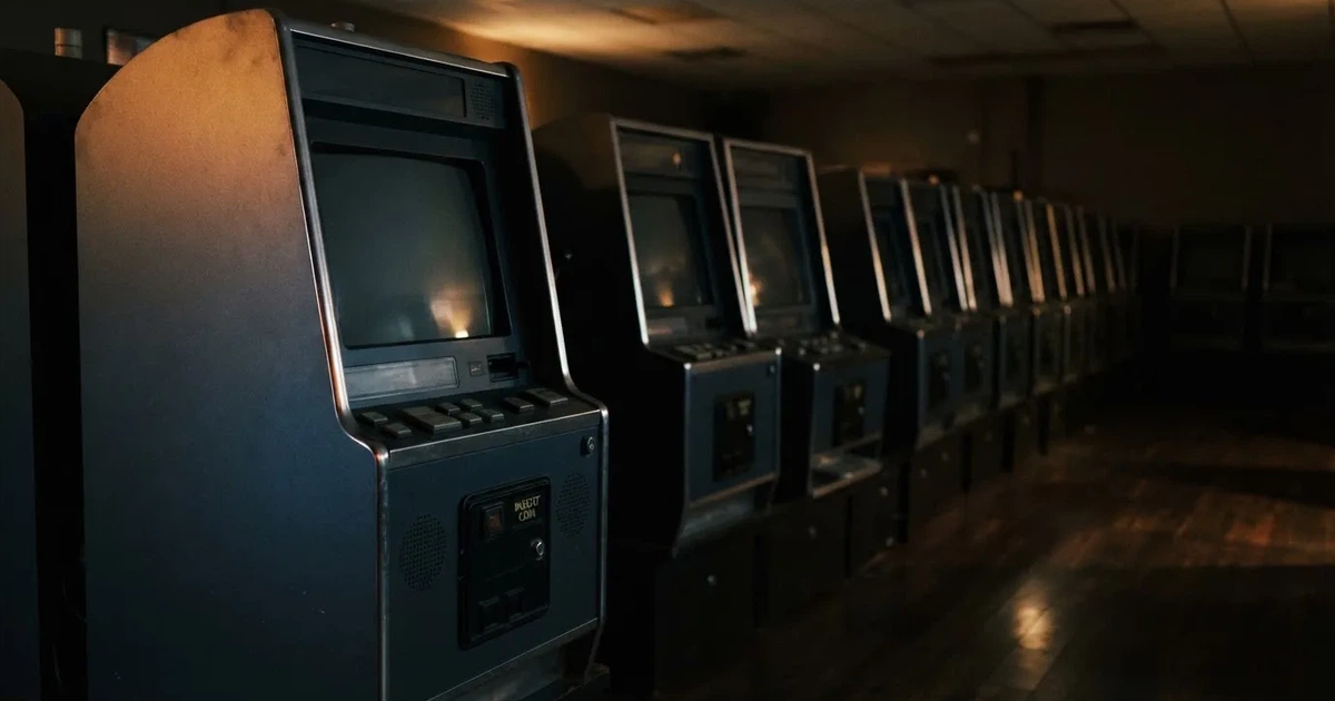 Rader av tomma spelautomater med släckta skärmar står uppställda i ett dimmat rum, fotograferat snett från sidan.